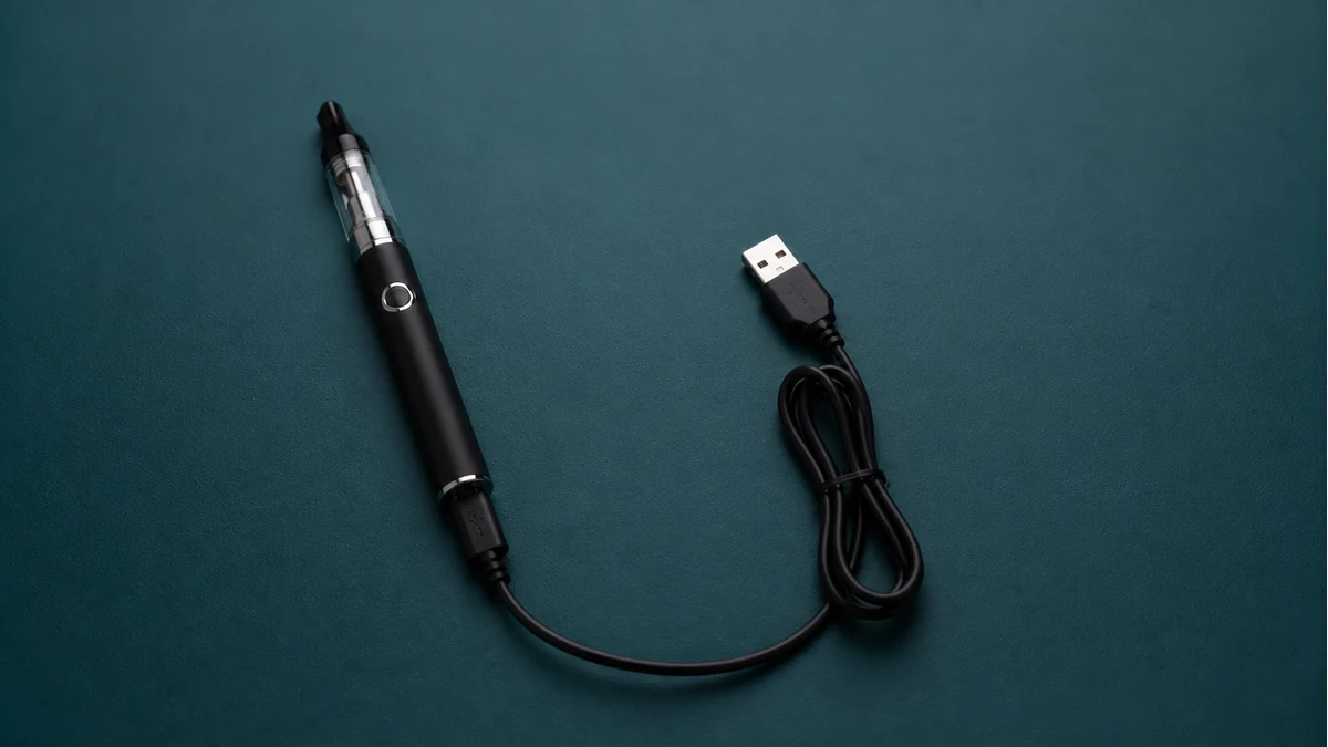 Vape pen battery charging beside its approved cable with full device visible