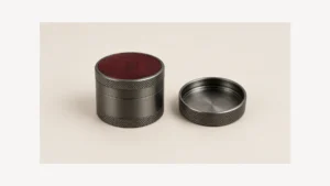 Closed metal herb grinder with burgundy top beside a separate plain cap