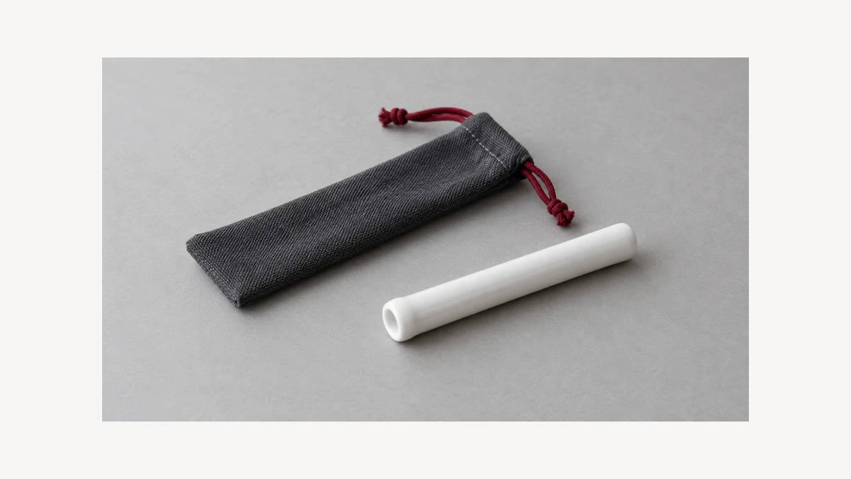 Plain white ceramic one hitter tube beside empty cloth sleeve